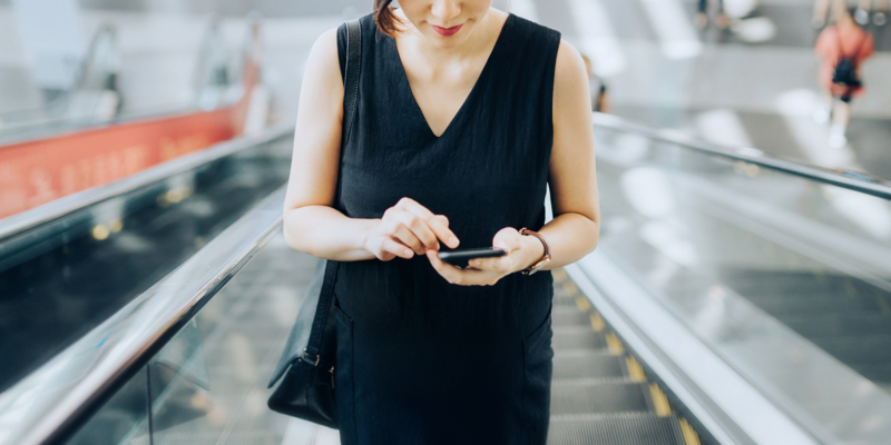 Young businesswoman reading emails on smartphone while riding on escalator