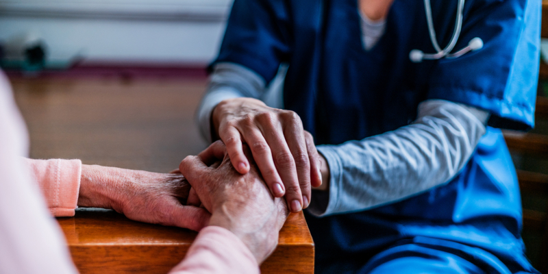 Close-up of senior woman and her home caregiver holding hands at home