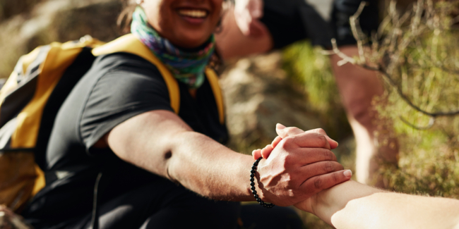 Cropped shot of two young women reaching for each other's hands on a hiking trail