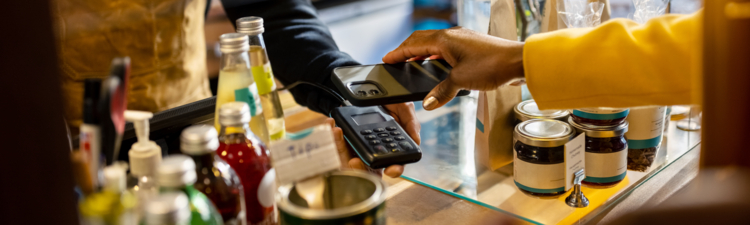 Cropped shot of a female customer using a smartphone for contactless payment. Cafe owner and customer at the checkout counter in a coffee shop.