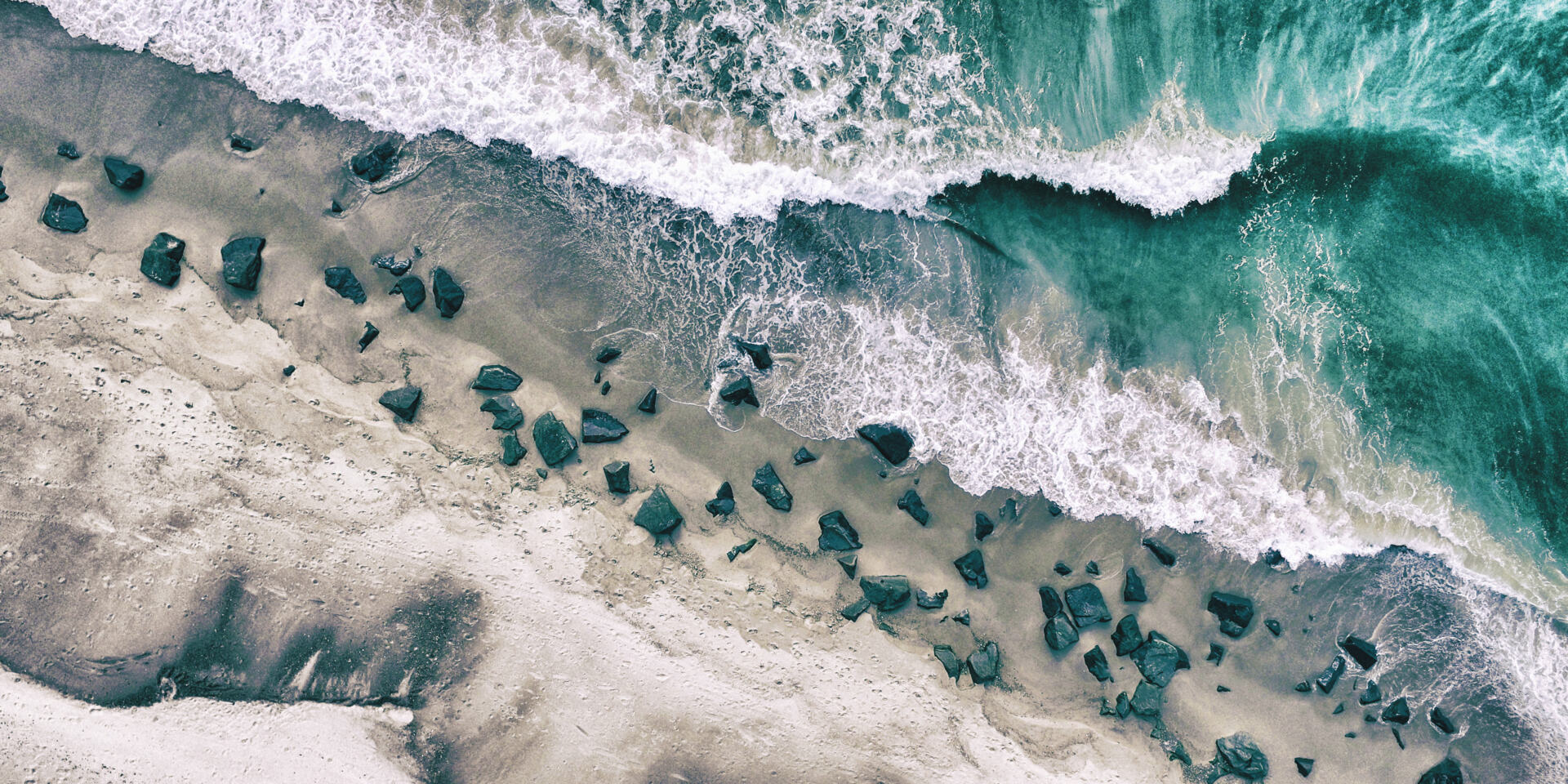 The sea with waves and ripples and the shore with rocks. This image was photographed from above with a drone.