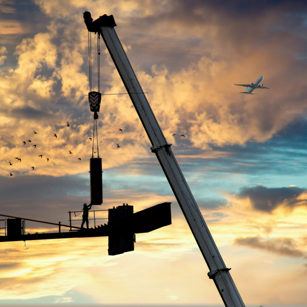 construction crane being built using a secondary crane shot against white sky with the concrete slab counterweight being placed and installed by a man holding it and guiding it in